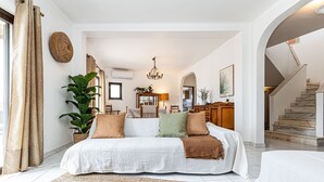 A spacious living room with a large sofa, a coffee table, and a dining area with a chandelier. - Casa do Vale PET Friendly Pool Lagoa Retreat (Lagoa)