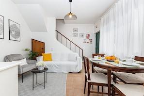 Ein modernes Wohnzimmer mit Sofa, Esstisch mit Stühlen, Treppe und einer Pendelleuchte.