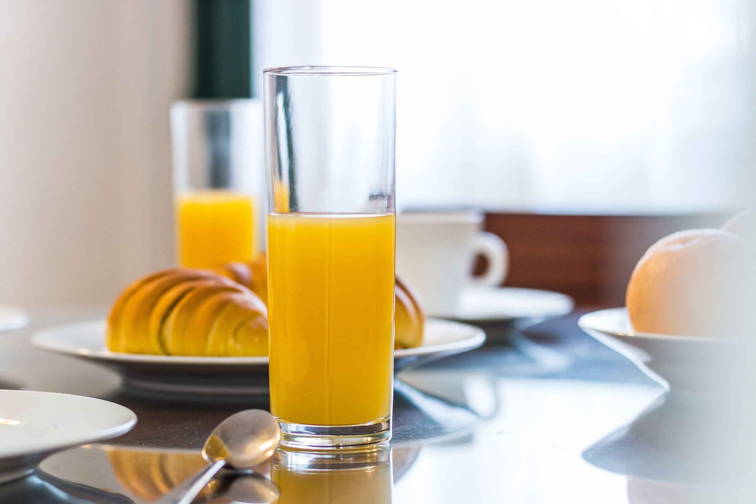 Une table mise pour le petit-déjeuner avec un verre de jus d’orange, des croissants et une tasse blanche.