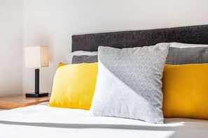 Un letto rifatto con diversi cuscini, una lampada da comodino e un comodino in legno.