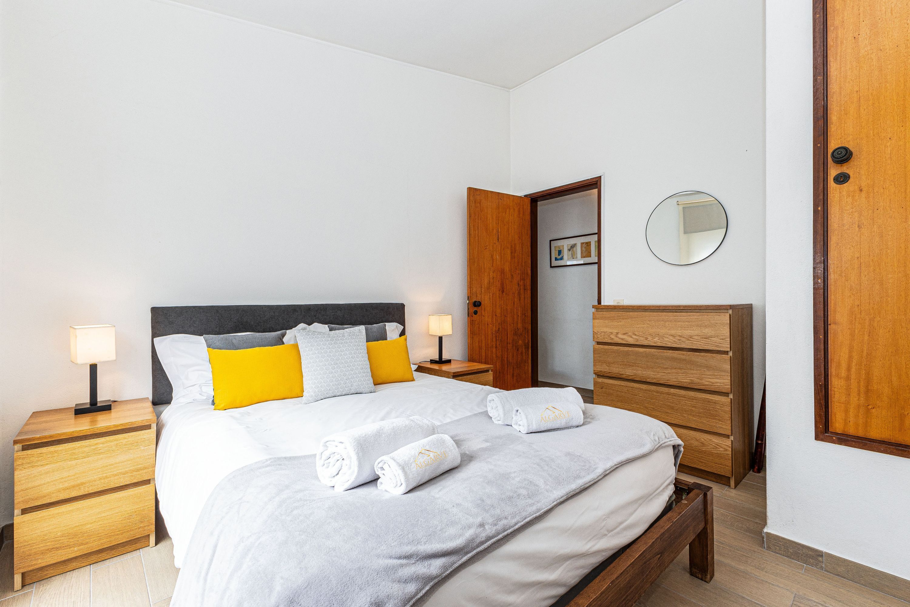 A bedroom with a bed, nightstands, a wooden dresser, a mirror, and a door.