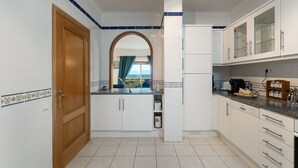 Cozinha com armários brancos, porta de madeira e vista através de um arco.
