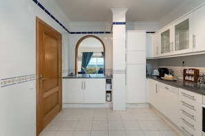 A kitchen with white cabinets, a wooden door, and a view through an archway. - Meia Praia Beach Golf Perfect for Families Ent (Lagos)