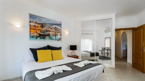 Quarto de hotel com cama, uma pintura, uma escrivaninha e um banheiro visível através de uma porta aberta.