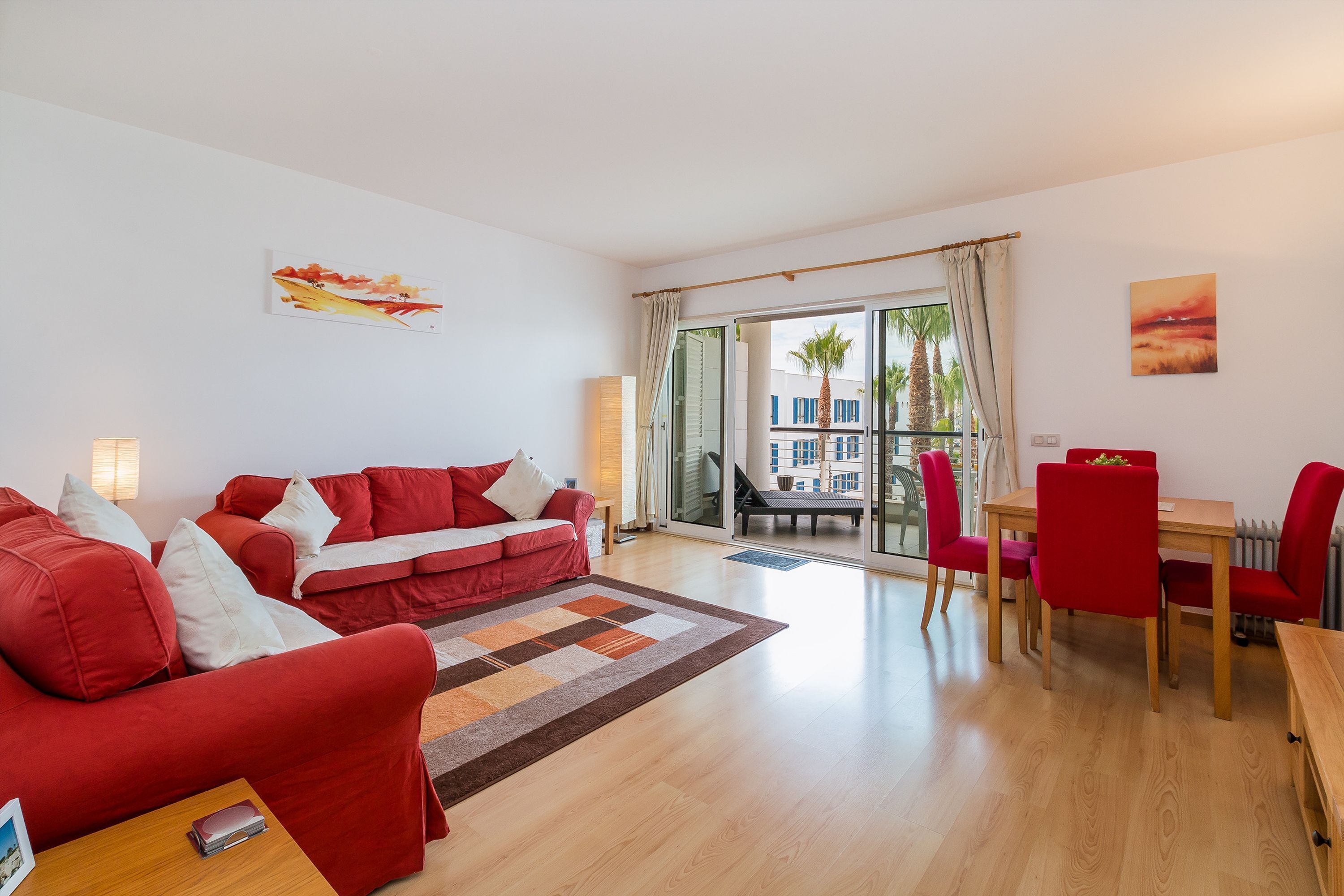 Ein Wohnzimmer mit einem roten Sofa, einem Esstisch mit roten Stühlen und Blick durch eine Glastür.