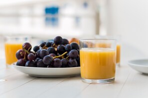 Eine Schale dunkellila Trauben und ein Glas Orangensaft auf einem weißen Tisch.