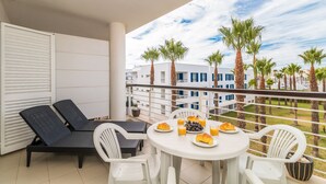 A balcony with a table set for breakfast, including croissants and orange juice, and a view of palm trees and buildings. - D Duarte On the Marina City Center and Beach (Lagos)