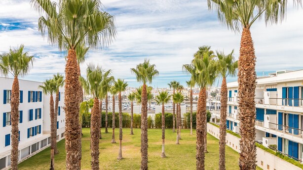 A courtyard with palm trees, a white building with blue shutters, and a view of the sea. - D Duarte On the Marina City Center and Beach (Lagos)
