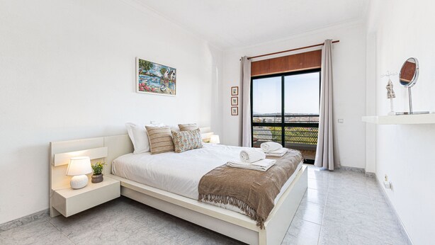 A bedroom with a bed, bedside table, lamp, and a painting on the wall. - Lagos Sea View Near the City Center (Lagos)