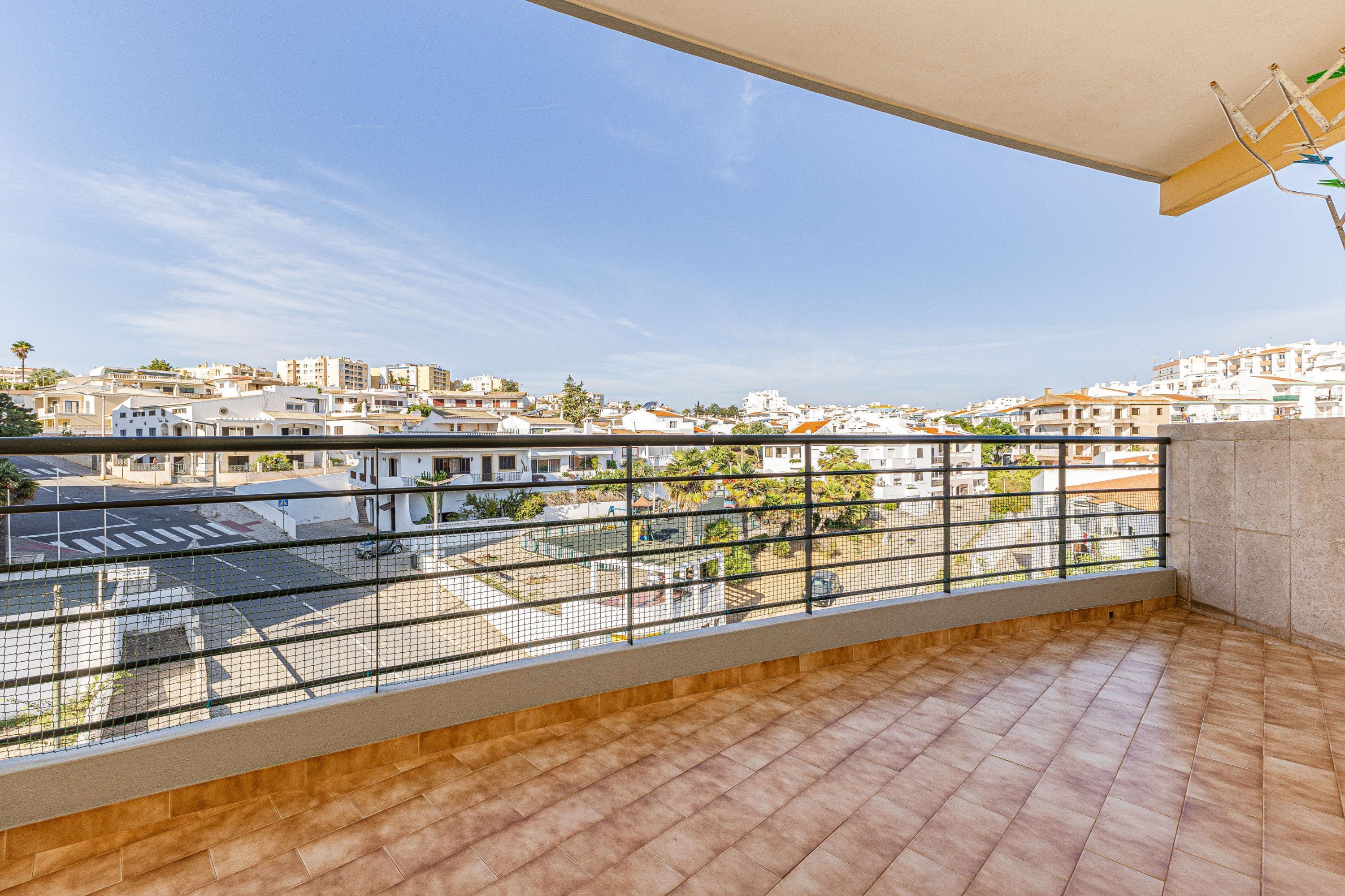 A balcony with a view of a residential area, a tiled floor, and a metal railing.