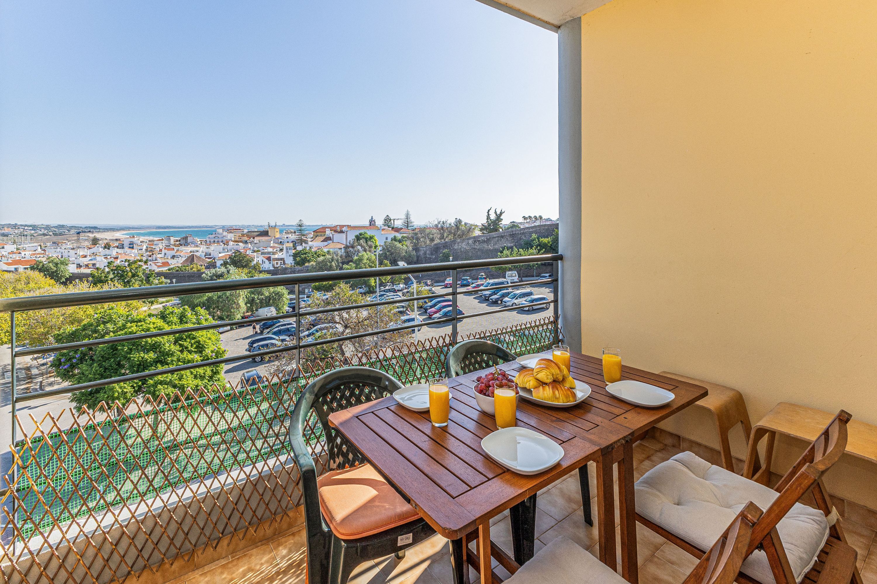 Een balkon met een ontbijtje gedekt, met uitzicht op een kuststad.
