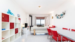 A modern room with a sofa, dining table, red chairs, a TV, and a window with a view. - Lagos Sea View Near the City Center (Lagos)