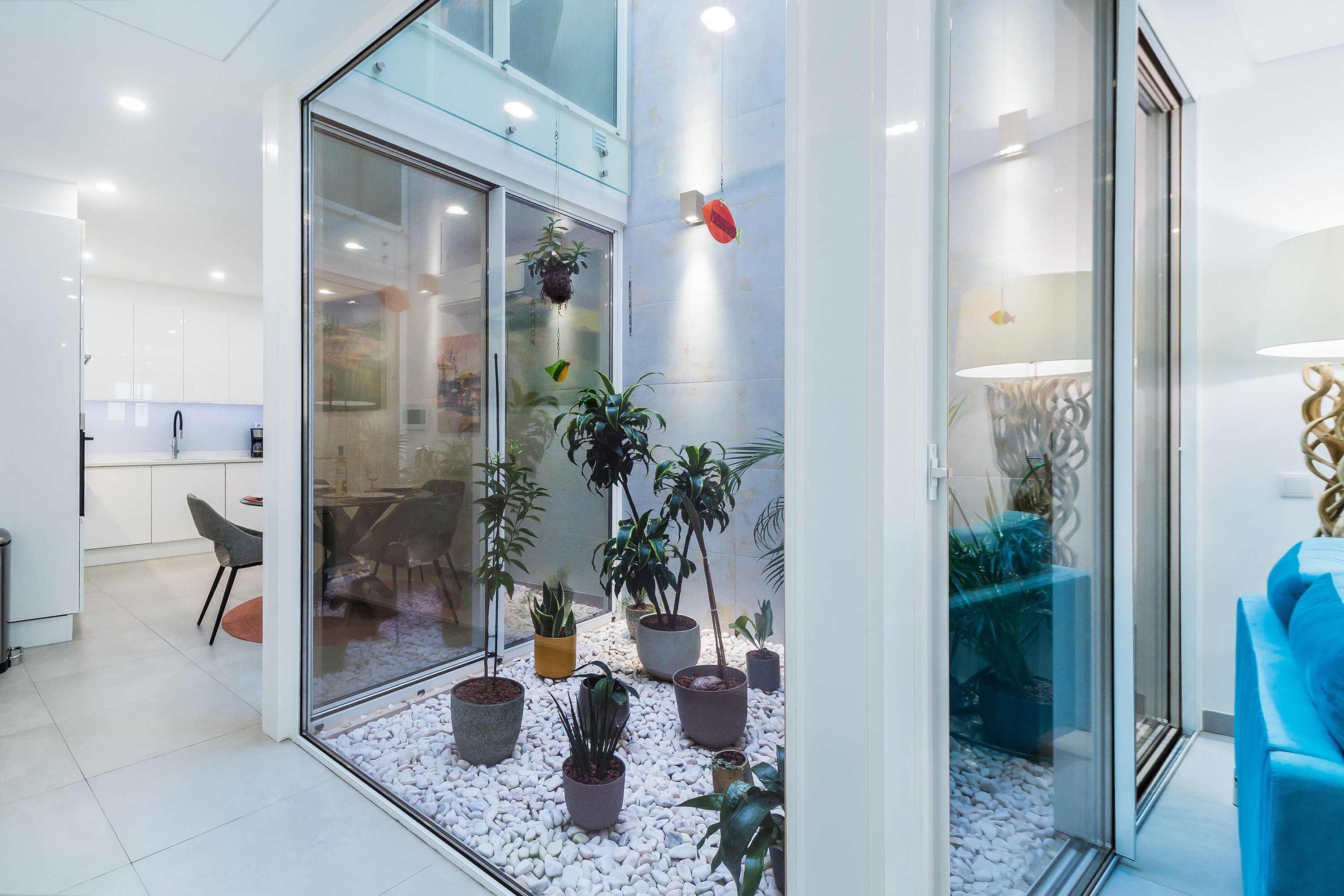 A modern interior with a glass partition, potted plants, a dining area, and a blue sofa.