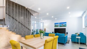 En moderne stue med et træspisebord, gule stole, blå sofaer og en trappe med gelænder af glas.