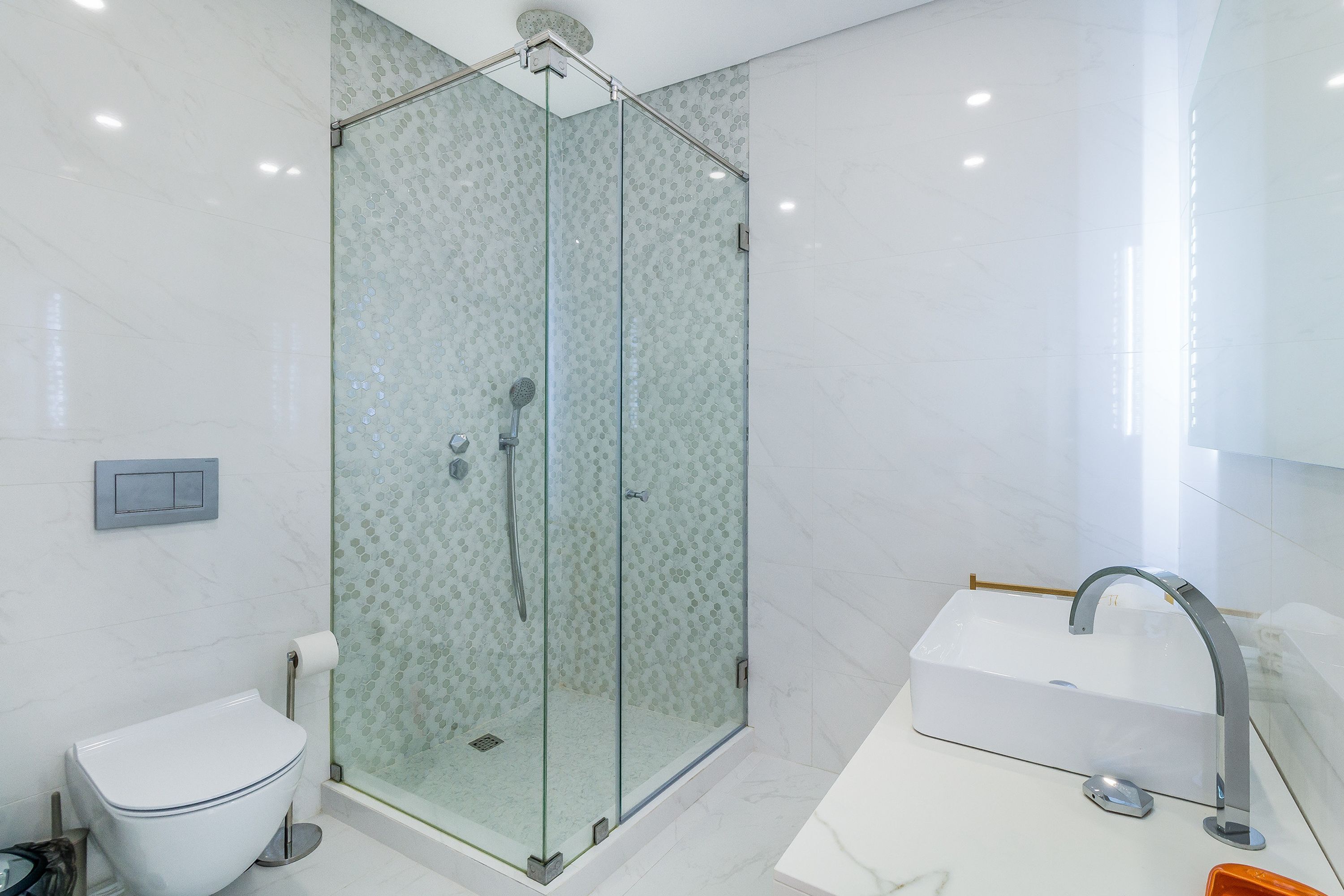 Une salle de bain moderne avec une douche à parois de verre, des toilettes blanches et un lavabo avec un robinet.