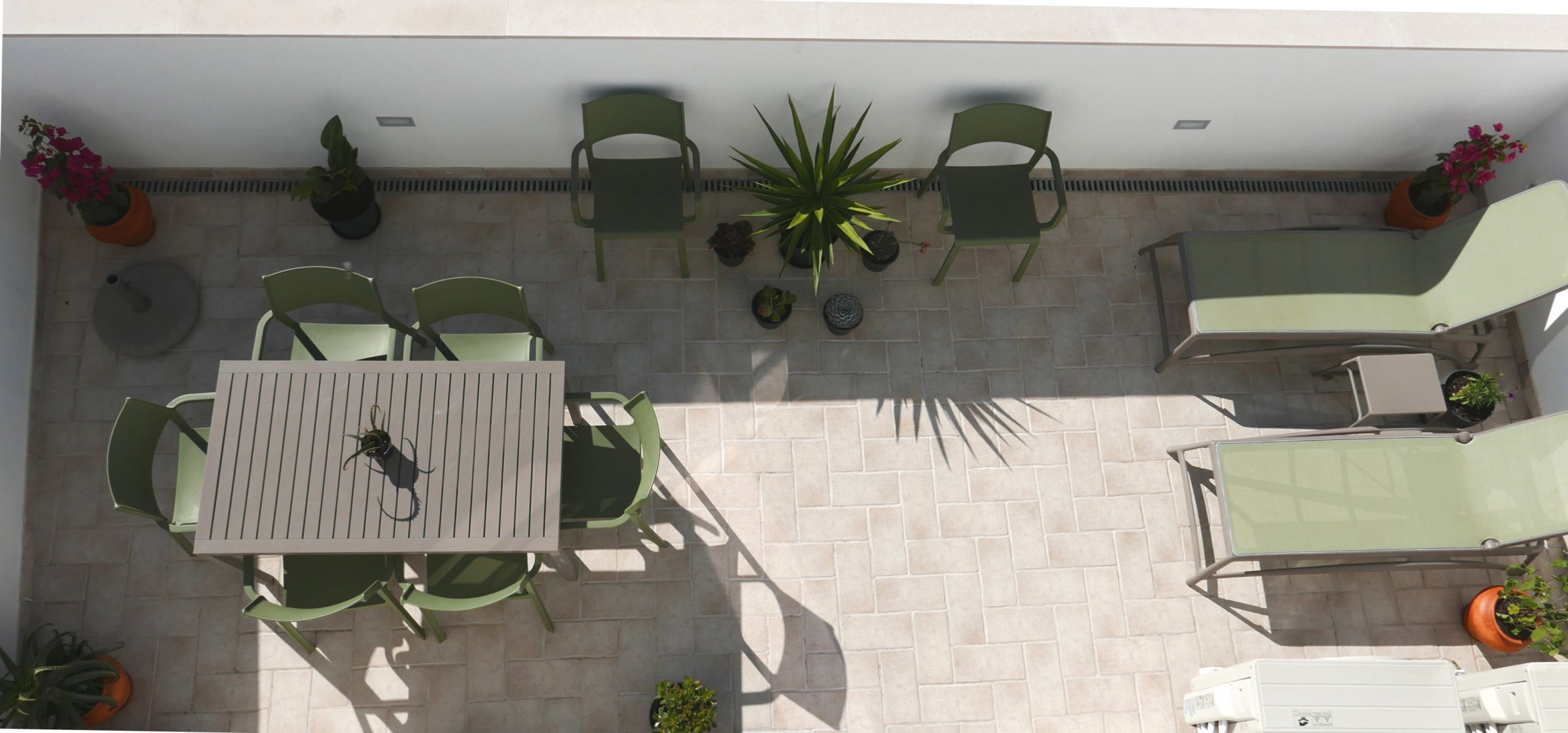 Une terrasse avec une table et des chaises, entourée de plantes en pot et dotée d’un sol carrelé.