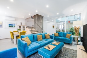 A modern living room with a blue sofa, a dining table with yellow chairs, a staircase, and a large window. - Vista Bonita Dowtown Family (Lagos)
