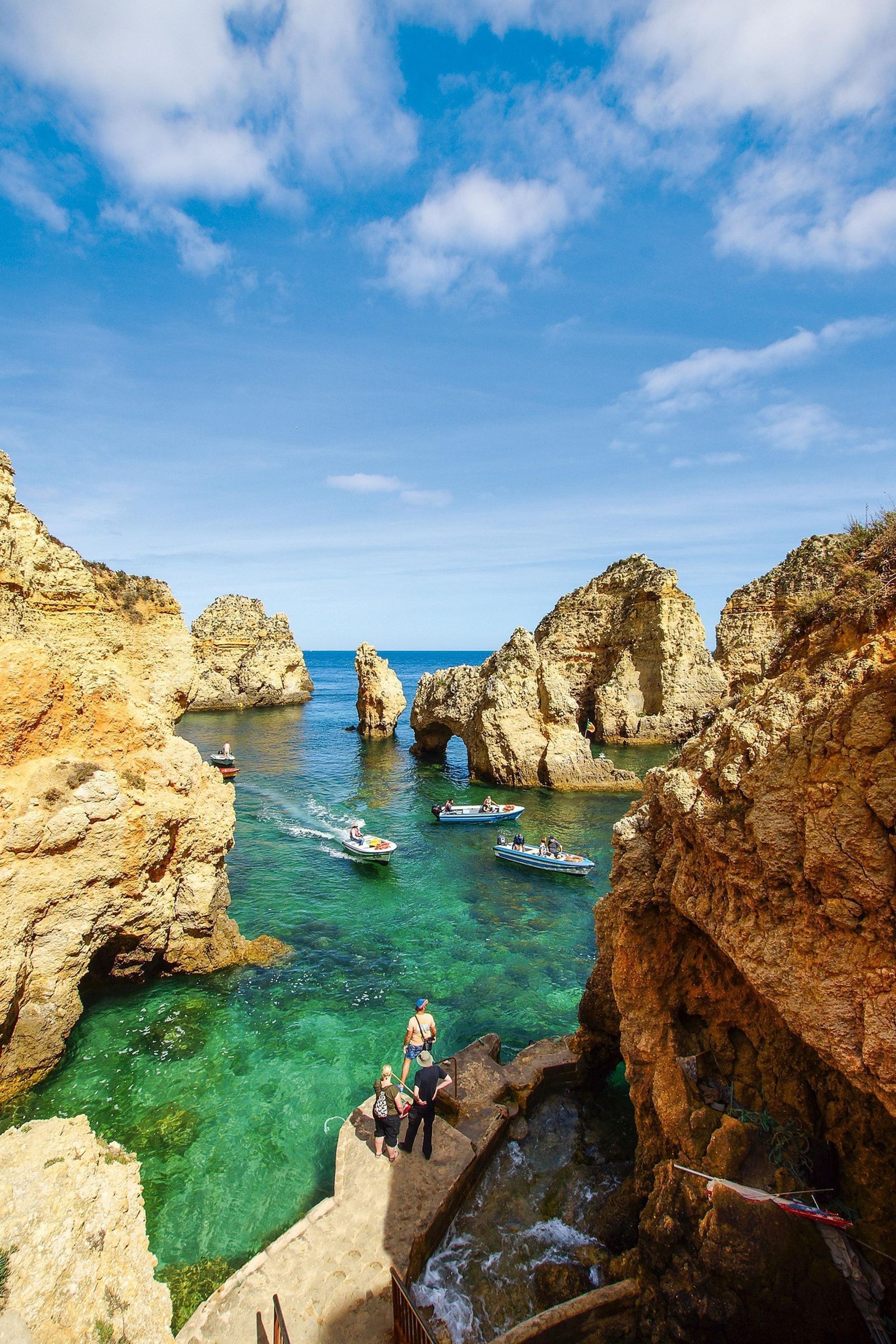 Un paysage côtier caractérisé par des falaises rocheuses, une eau d’un bleu limpide et la présence de bateaux.