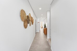 A modern hallway with a neutral color palette, featuring a series of woven wall art and a wooden side table with a vase. - Ria Terrace House in Alvor (Portimão)