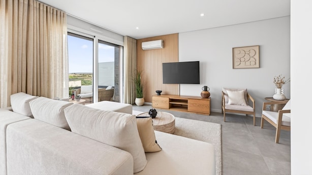 Ein modernes Wohnzimmer mit einer Couch, einem Fernseher und Blick ins Freie.