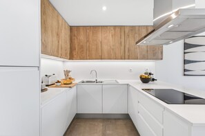 Una cocina moderna con armarios blancos, un muro decorativo de madera, una estufa empotrada y un fregadero.