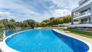Ein moderner Pool mit Glasgeländer, umgeben von einem gepflegten Rasen und einem zeitgemäßen Gebäude.