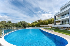 A modern swimming pool with a glass balustrade, surrounded by a well-maintained lawn and a contemporary building. - Ria Terrace House in Alvor (Portimão)