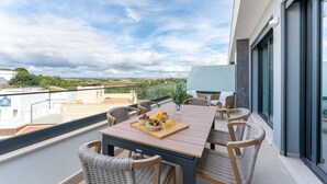 Ein Balkon mit einem Holztisch, Korbstühlen und einer Platte mit Obst und Saft.