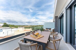 A balcony with a wooden table, wicker chairs, and a tray with fruit and juice. - Ria Terrace House in Alvor (Portimão)