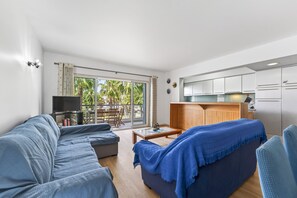 Ein modernes Wohnzimmer mit einer Couch, einem Couchtisch und einem Fernseher. Ein Balkon mit Tisch und Stühlen ist vorhanden.