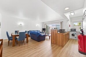 Una sala de estar moderna con sofá, mesa de comedor y sillas, una cocina equipada y un área de lavandería.