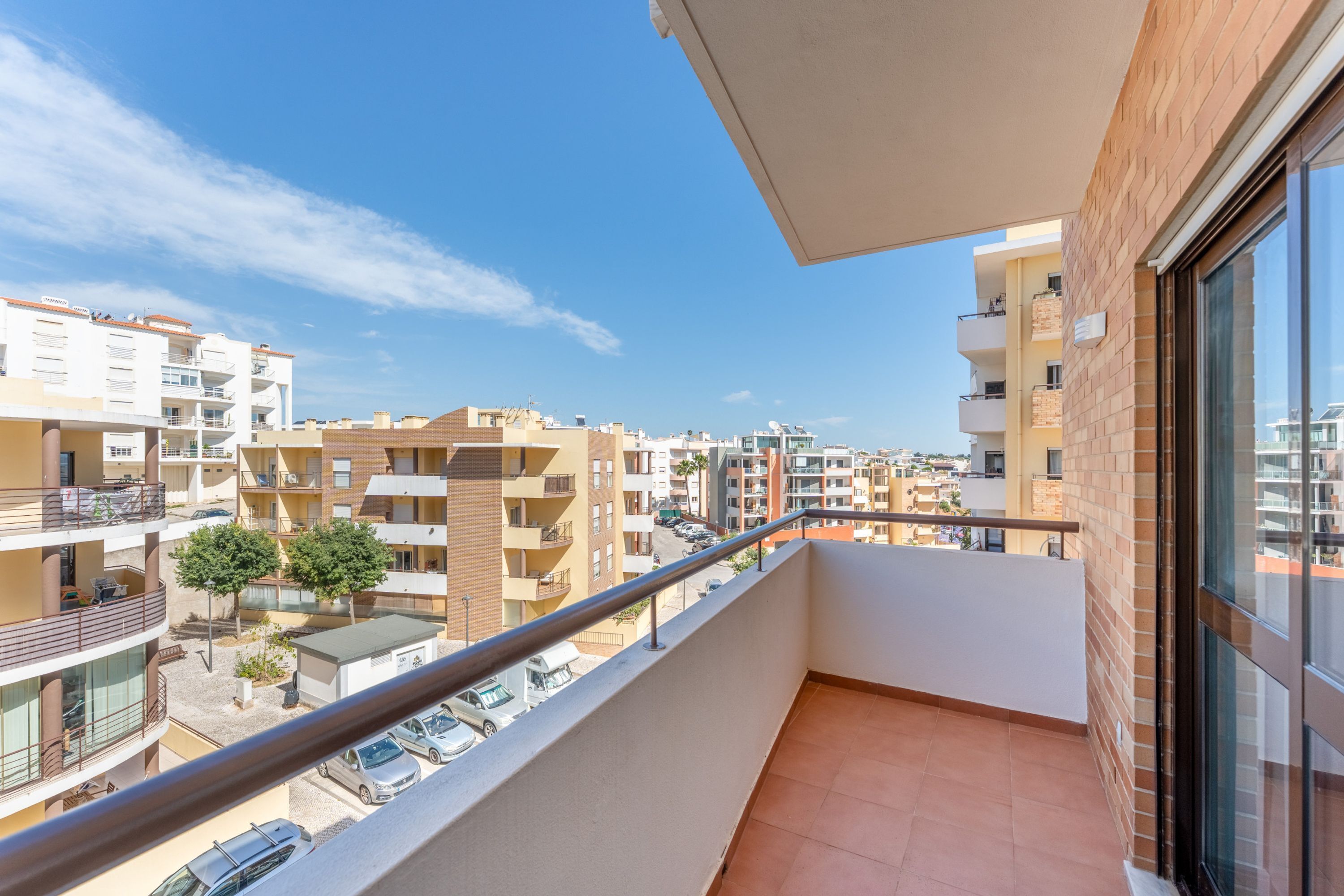 A balcony with a view of neighboring buildings and parked cars.