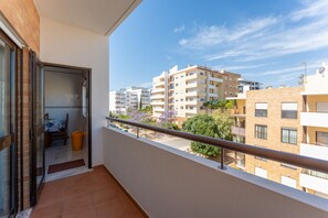 Ein Balkon mit Blick auf Wohnhäuser, eine Tür zu einem Innenraum und ein Mülleimer.