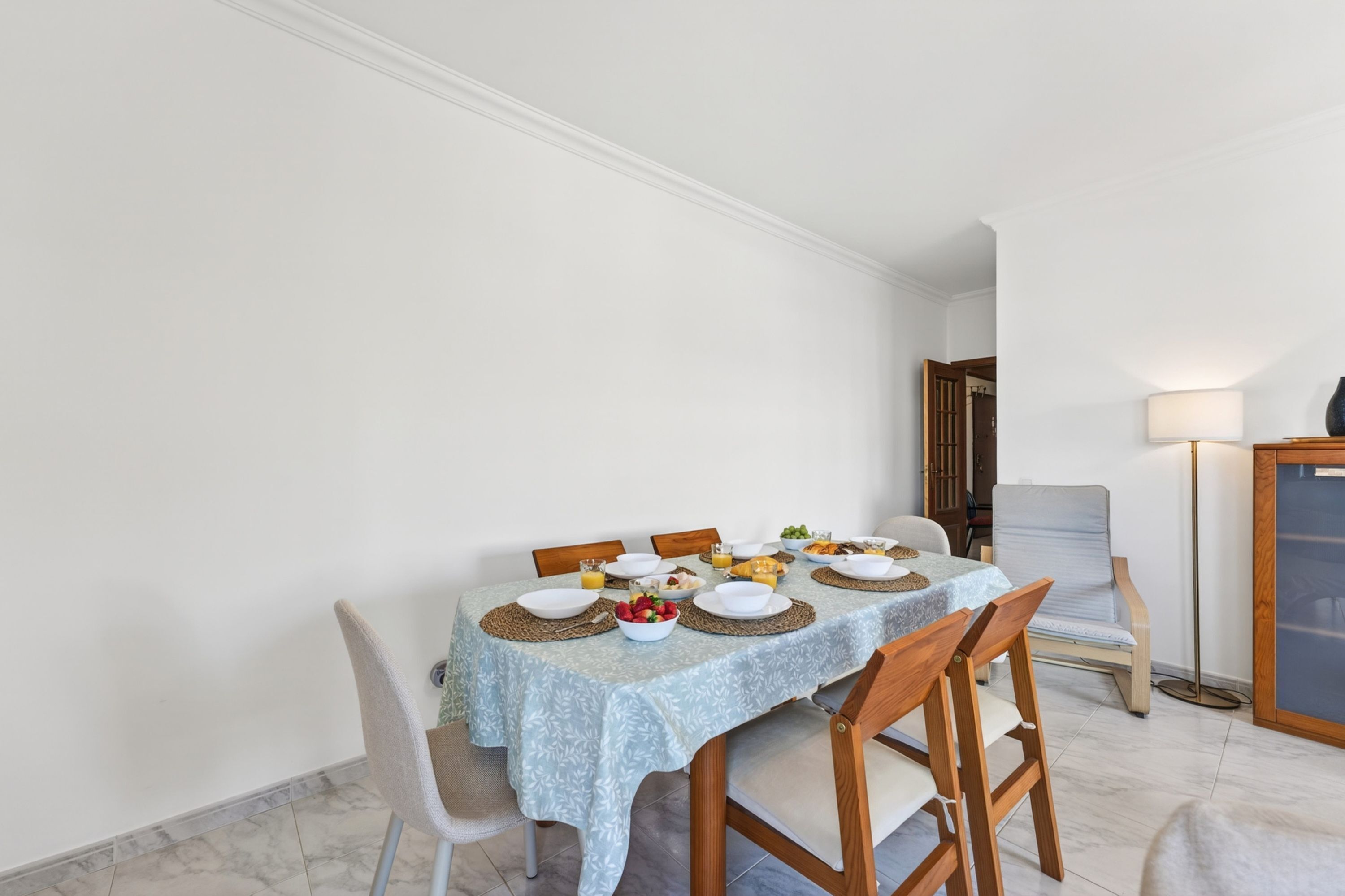 A dining area with a table set for four, chairs, a lamp, and a vase on a side table.