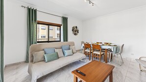 Ein Wohnzimmer mit einer Couch, einem Esstisch, Stühlen und einer Fernbedienung auf einem Couchtisch.