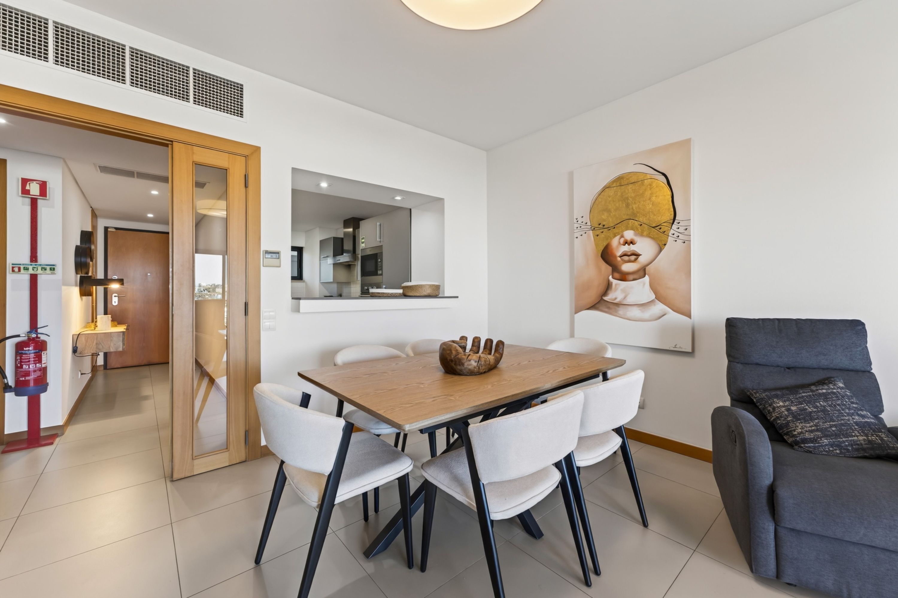 A modern dining area with a wooden table, white chairs, and a grey sofa.