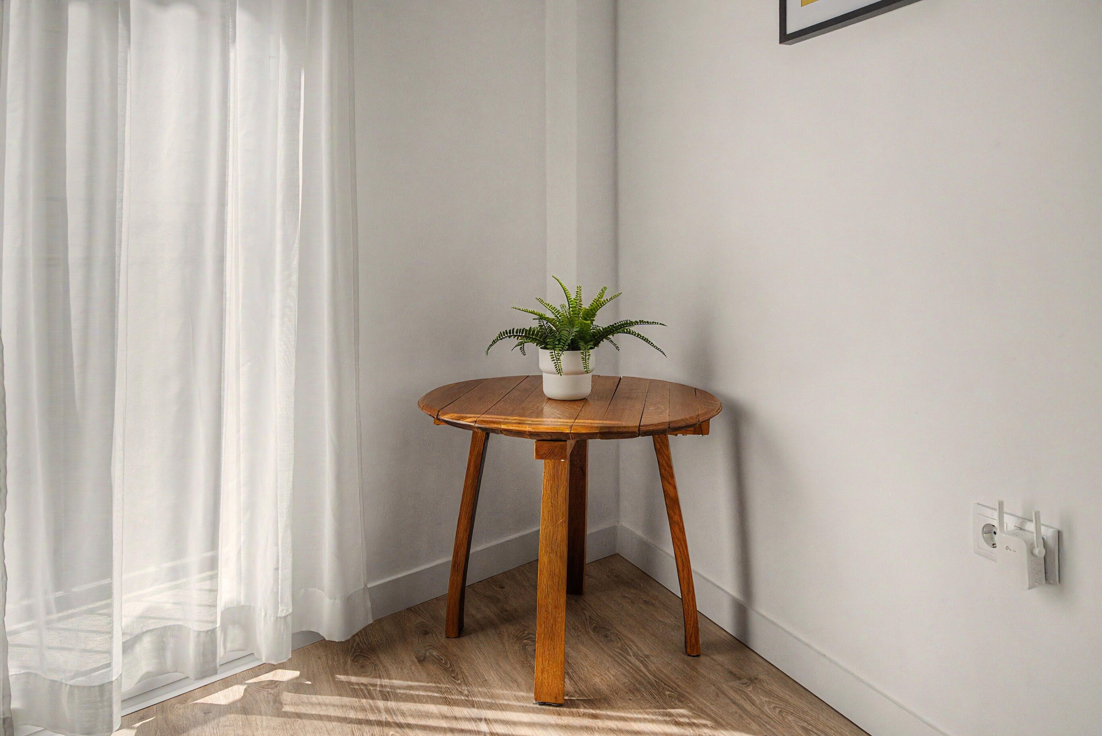 A corner of a room with a wooden table, a potted plant, and a white wall.