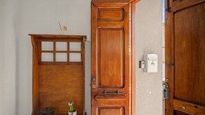 A wooden door with a glass panel and a metal handle, a small shelf with a basket and a plant, and a white electrical box on the wall.