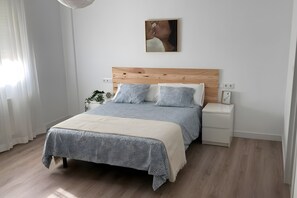 A neatly arranged bedroom with a wooden headboard, a bed with grey bedding, a bedside table, and a wall-mounted picture.
