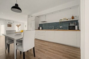 A modern kitchen with white cabinetry, a wooden countertop, and a black pendant light.
