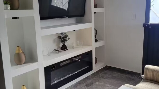 Ett vardagsrum med en platt-TV, en takfläkt, en soffa och ett soffbord.