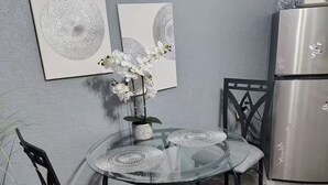 En matplats med ett glasbord, två stolar, en vas med vita blommor och två abstrakta målningar på väggen.