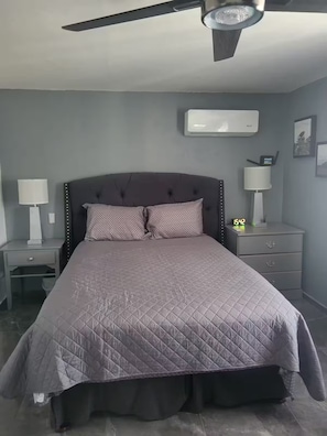 A bedroom with a bed, nightstands, a ceiling fan, an air conditioner, and a digital clock.