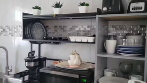 Ett kök med en mikrovågsugn, en kaffebryggare och en mixer på bänkskivan. På hyllan ovanför står krukväxter, och det finns ett handfat med en kran.