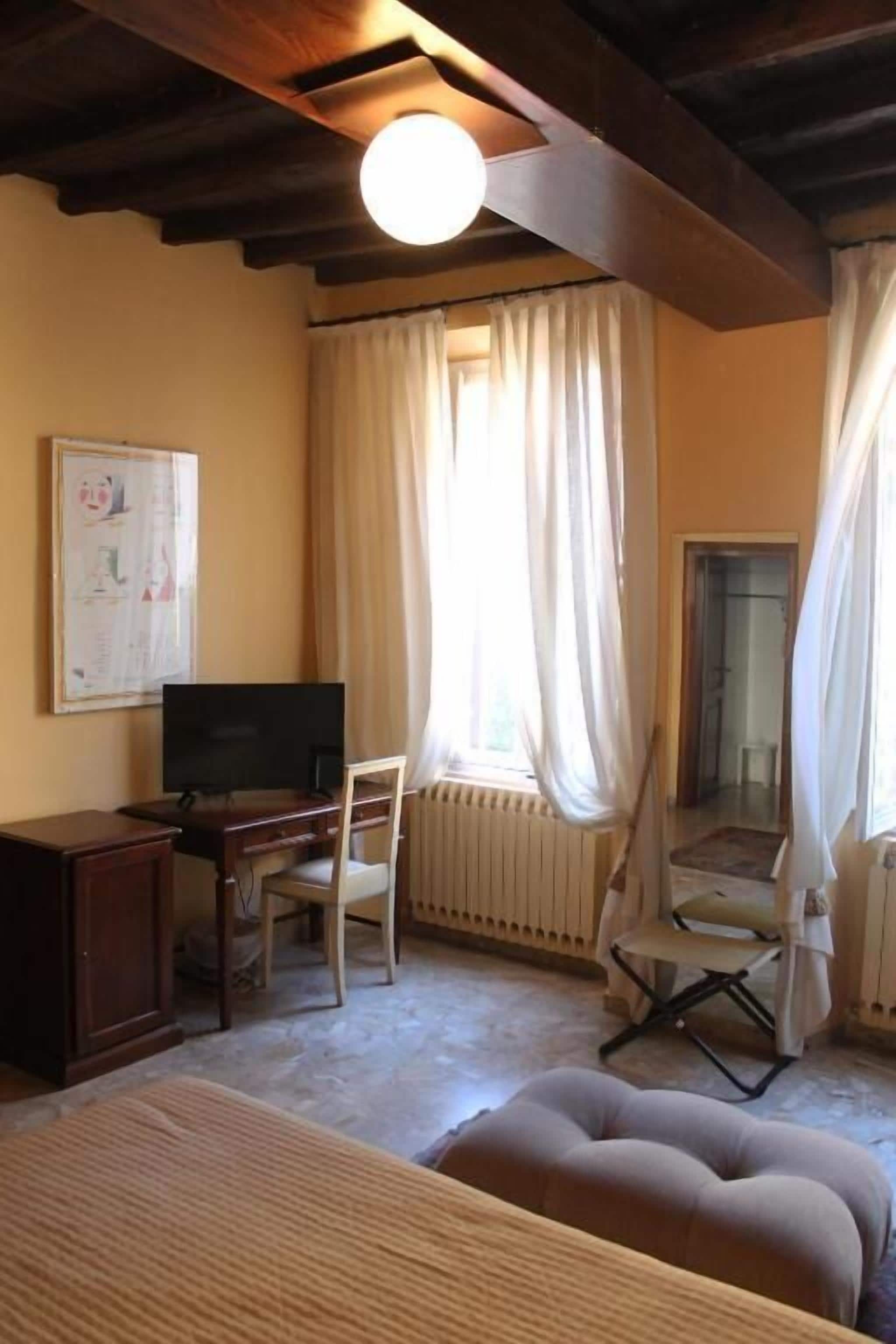 Ein Zimmer mit einem Bett, einem Schreibtisch mit Computer, einem Stuhl, einer Heizung und einem Fenster mit Vorhängen.