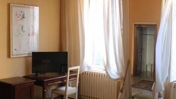 Ein Zimmer mit einem Bett, einem Schreibtisch mit Computer, einem Stuhl, einer Heizung und einem Fenster mit Vorhängen.