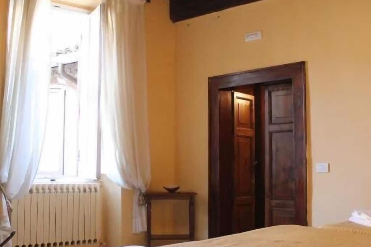 Une chambre à coucher avec un lit, une porte en bois, un radiateur et une fenêtre avec des rideaux.