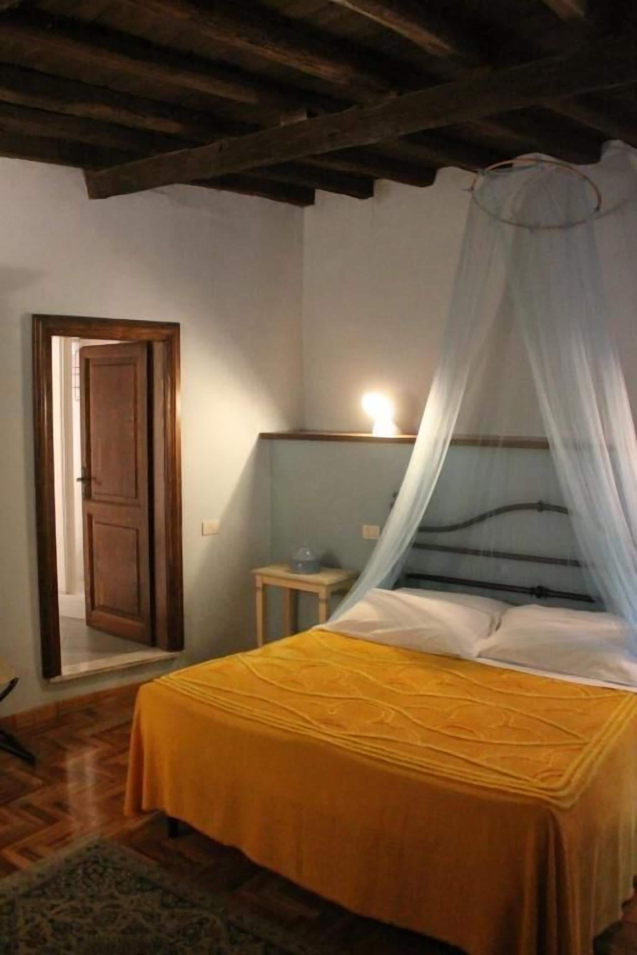 Un dormitorio con una cama, vigas de madera en el techo, una puerta y una mesita de noche.
