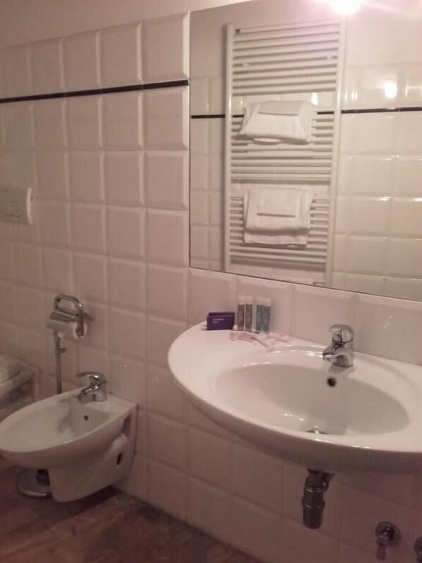 Un baño con lavamanos blanco, un bidé, un espejo y un perchero para toallas.