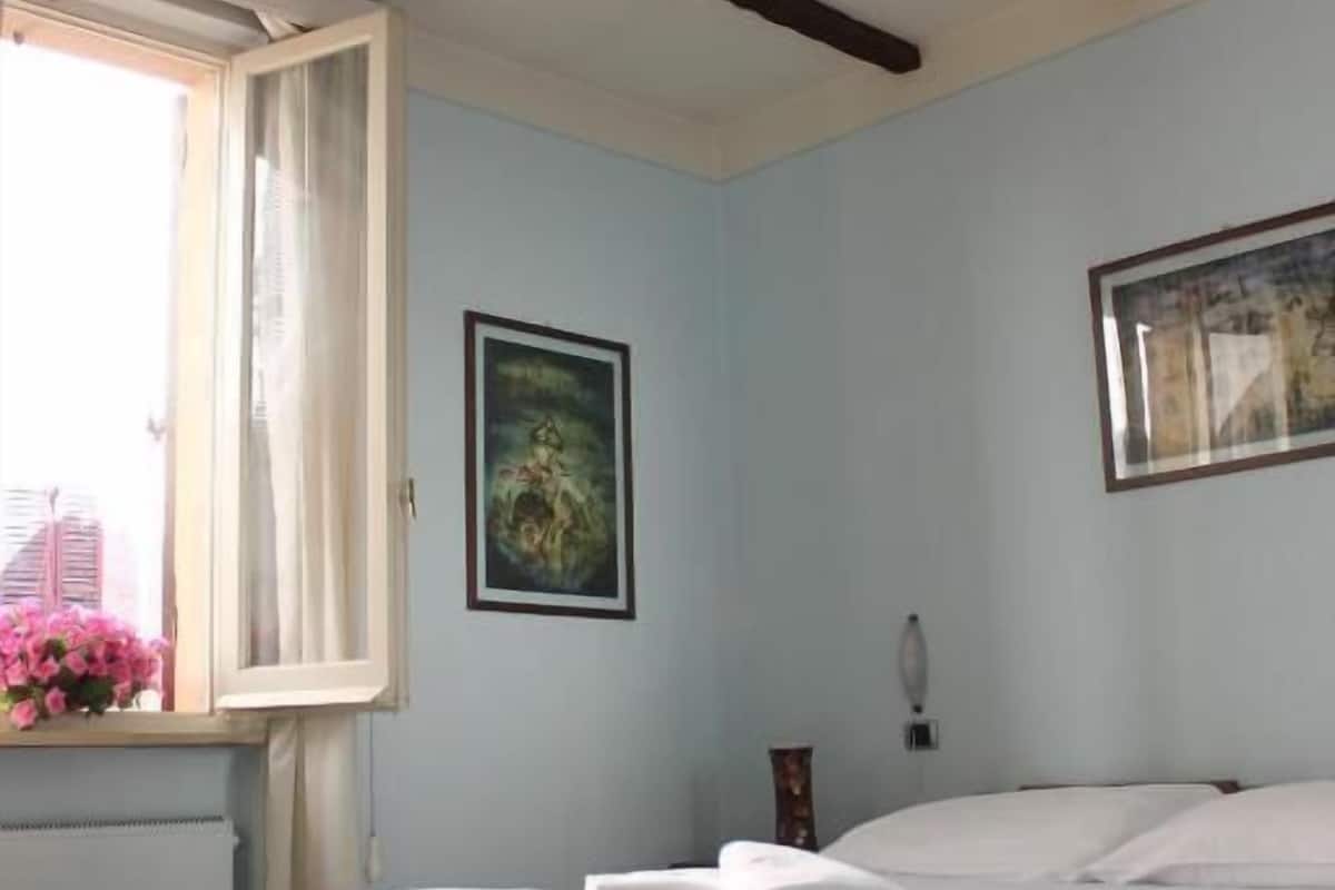 Une chambre à coucher avec un lit, une fenêtre avec des rideaux, un tableau encadré au mur et un luminaire au plafond.